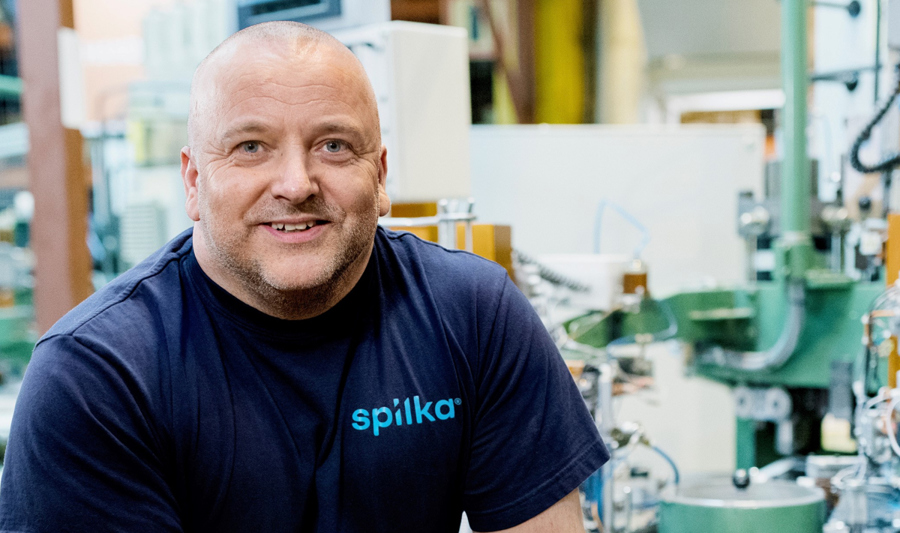 Arbeider i Spilka-fabrikken står smilende foran maskineri.